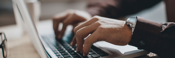 Close-up image of a man's hands typing on a laptop, browsing the Marsden's Online Savings FAQs.