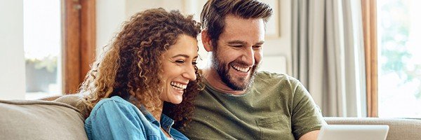 Couple sit on sofa looking at the Marsden website for a mortgage in Guernsey.
