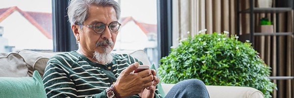 Mature man looks at RIO mortgage rates with Marsden Building Society in Guernsey on his phone.