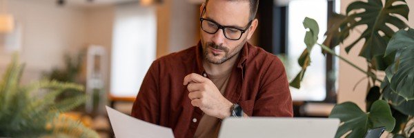 Man sat at table with a laptop and reading paper