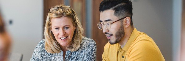 Colleagues sit at a desk and look at a laptop together, discussing Marsden's Workplace Savings scheme