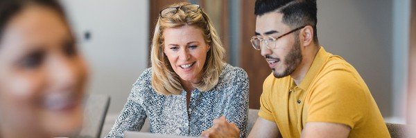 Colleagues sit at a desk and look at a laptop together, discussing Marsden's Workplace Savings scheme