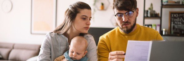 A young couple with a baby sat at a table in their home, managing their household budget and reviewing receipts.