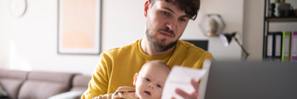 Dad holds baby on his knee as he reviews his finances