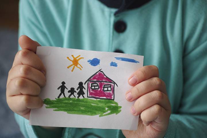 Child holds a drawn house with family.