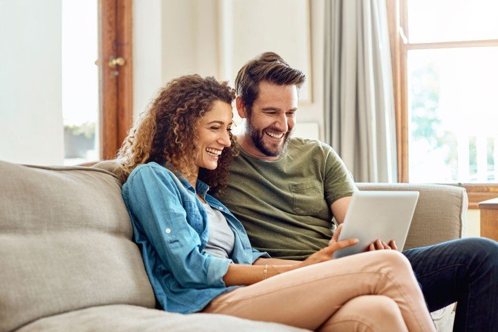 Couple sit on sofa looking at the Marsden website for a mortgage in Guernsey.