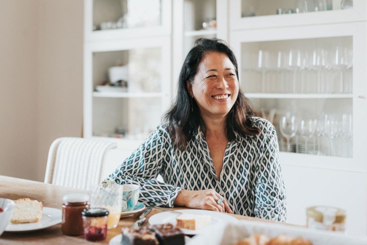 Smiling lady sat in her kitchen enjoying breakfast after reading Marsden's FAQs about mortgages in Guernsey.