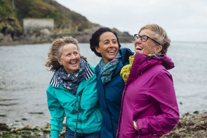 Three older women smiling together in front of the sea