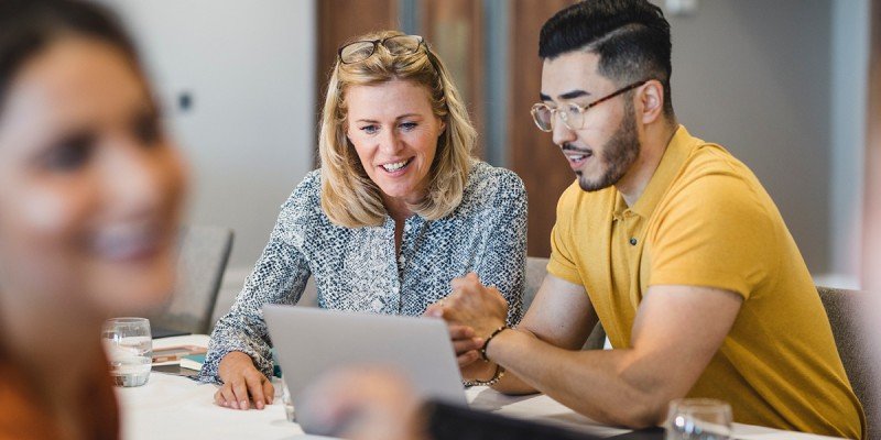 Colleagues sit at a desk and look at a laptop together, discussing Marsden's Workplace Savings scheme