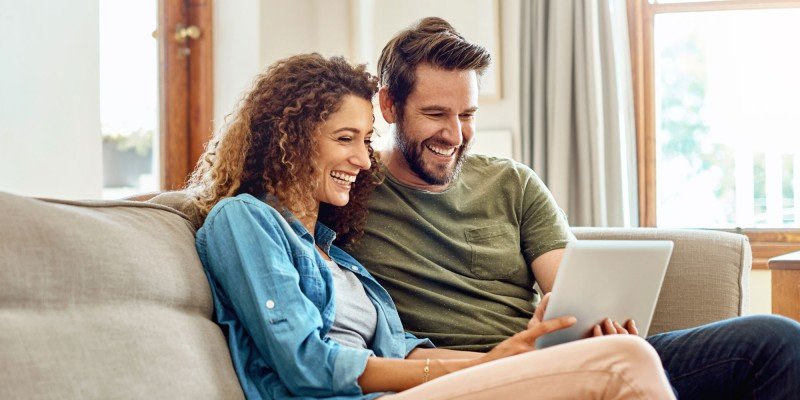 Couple sit on sofa looking at the Marsden website for a mortgage in Guernsey.