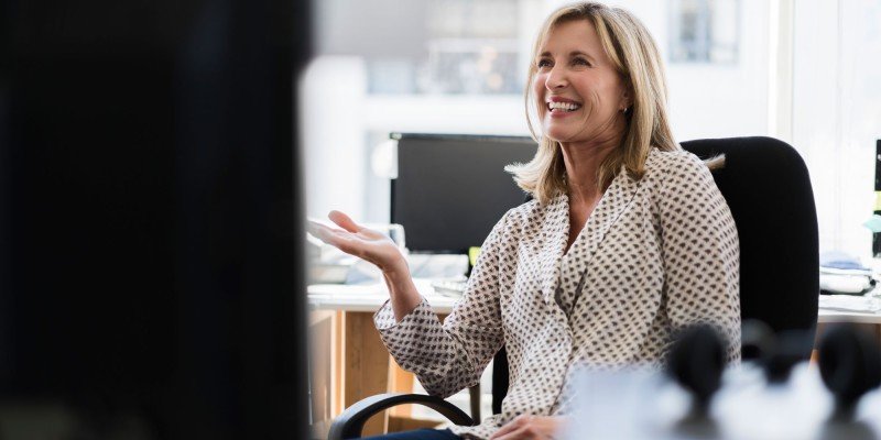 Smiling middle-aged woman enjoys a conversation with a colleague in her office.