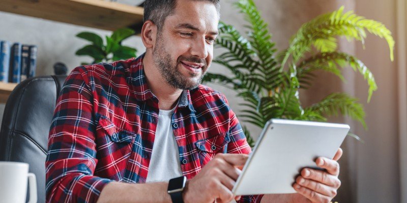 Man smiling at tablet indoors while renewing home insurance